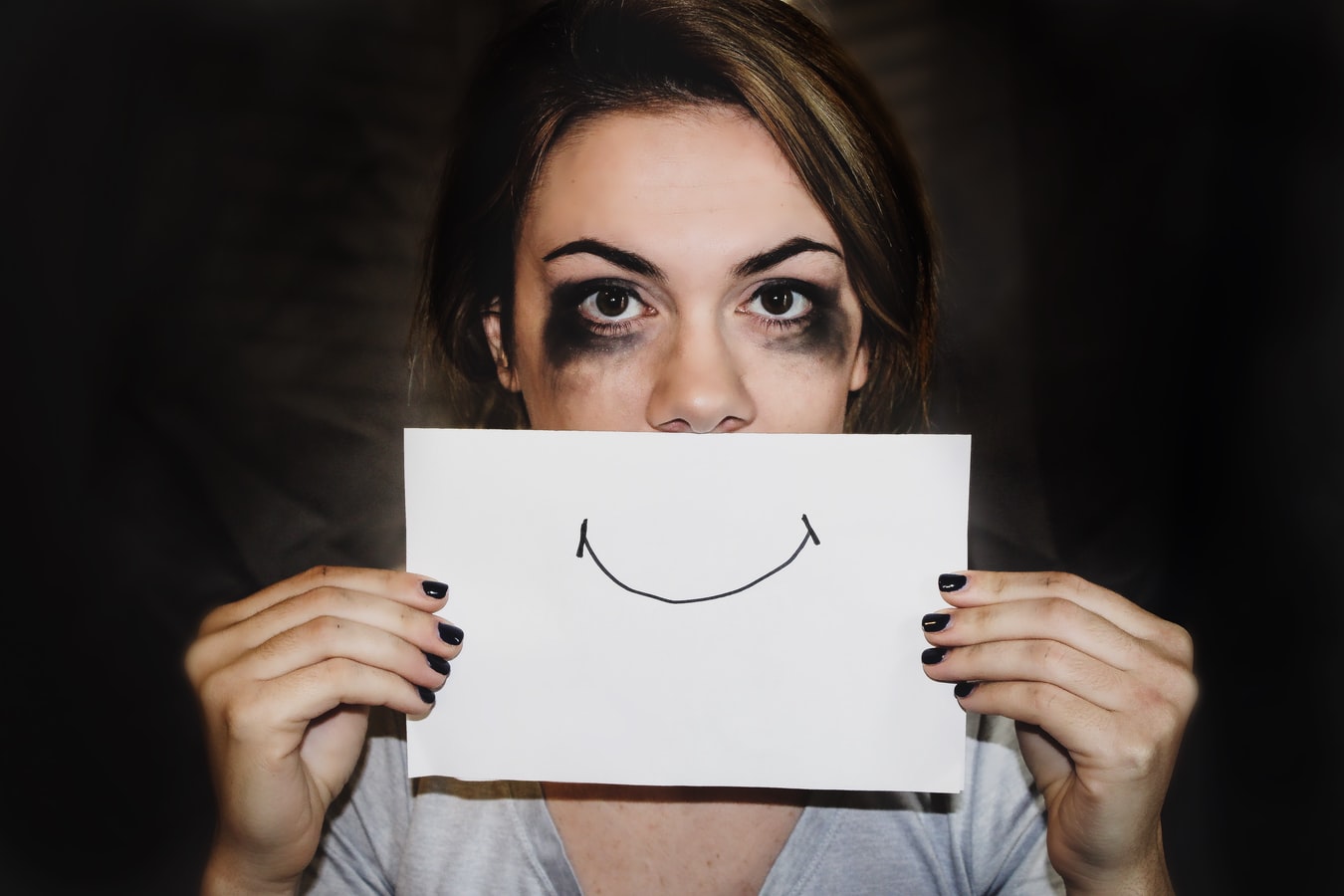 Une femme battue tenant une feuille representant un sourire contraint.